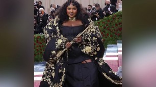 '#Lizzo playing a gold flute in her black & gold #ThomBrowne dress & coat set | #MetGala 2022'